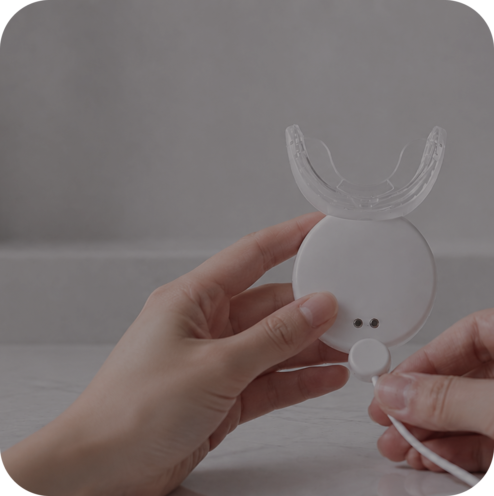 Hands holding the HealRay device with its magnetic charging cable